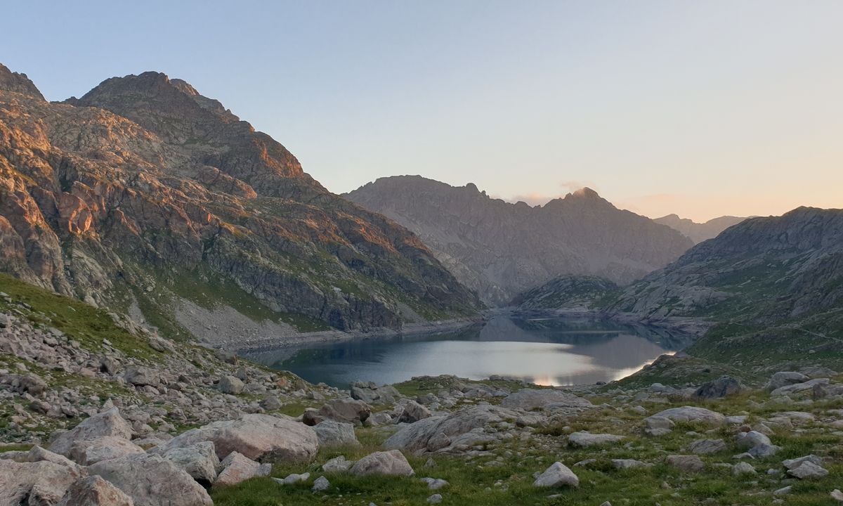 A calm mountain lake reflecting the surrounding peaks at dawn
