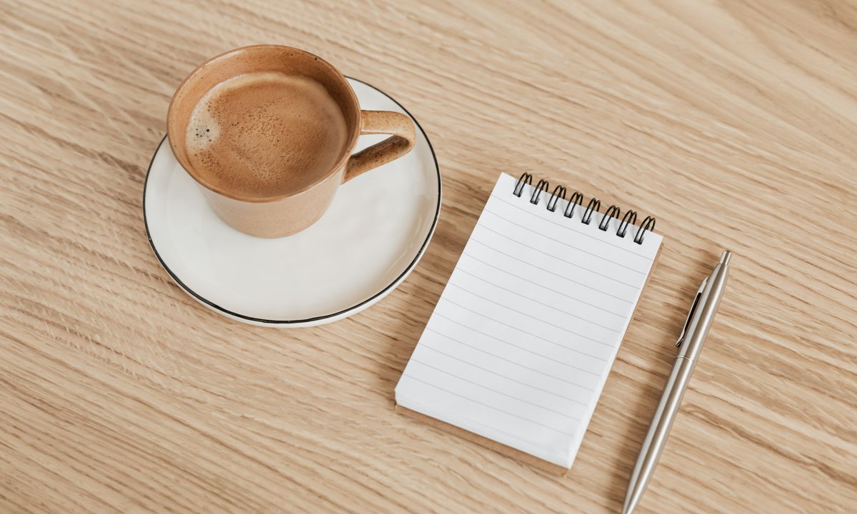 Open notebook, pen and a cup of coffee on a wooden desk