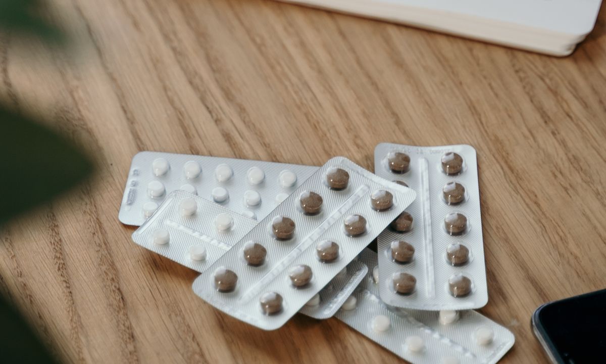 Medication blister packs beside an open notebook on a wooden desk