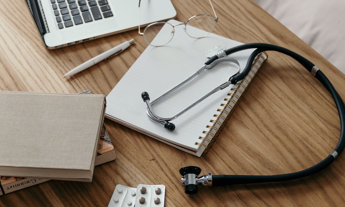 A stethoscope, medication and a notebook arranged on a work desk