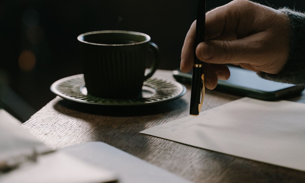 An open journal, writing pen, and coffee on a wooden desk
