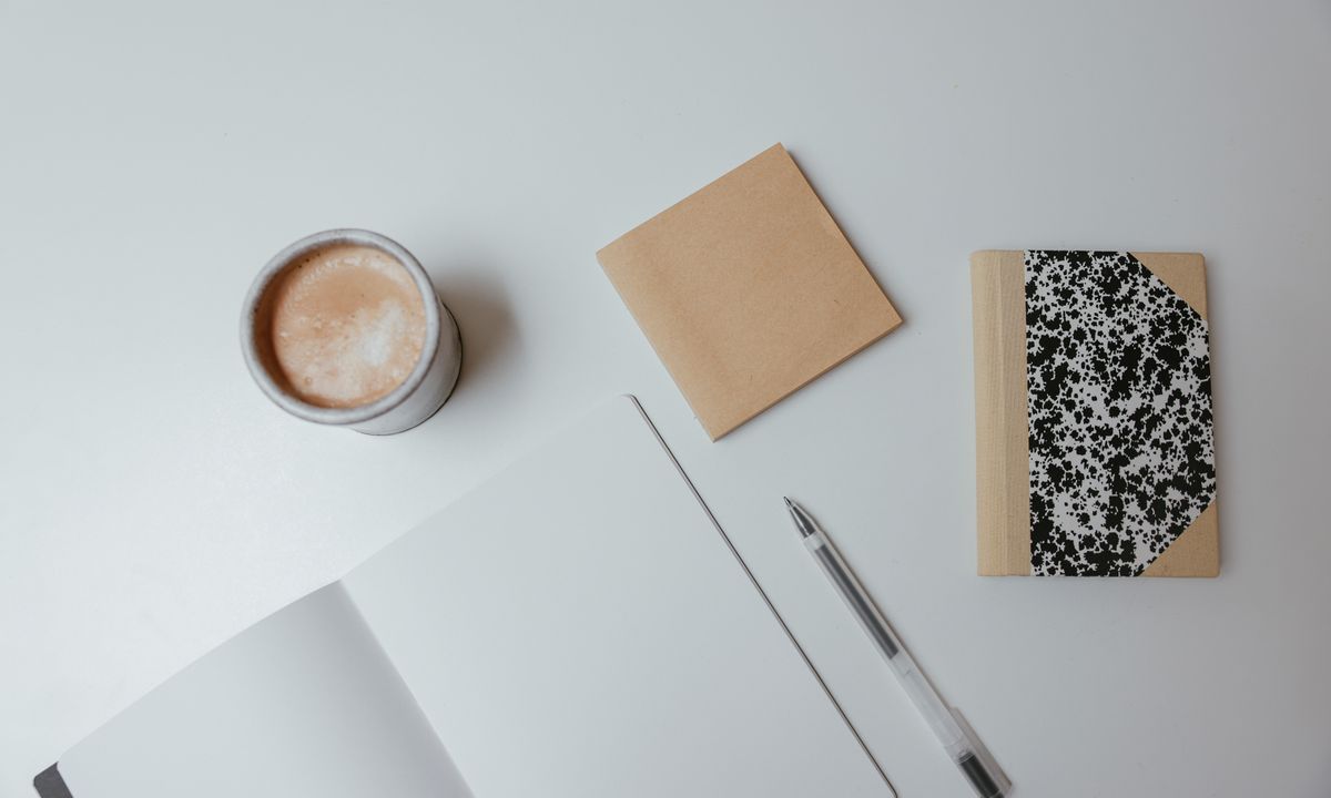 Notebooks and a cup of coffee arranged on a light-colored desk